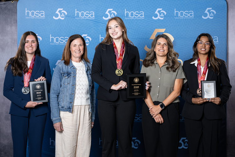 Five people stand in front of a HOSA banner. Three of them wear a medal and hold an award plaque.