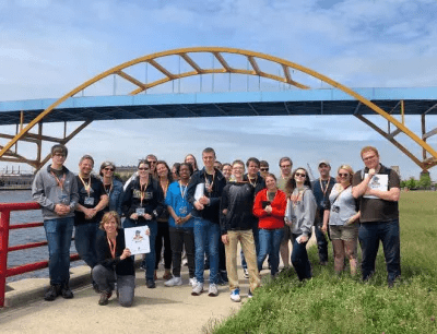 A group of 20 people posing outside in front of a bridge.