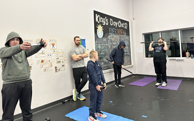 Four youths lift weights while an adult supervises in the background.