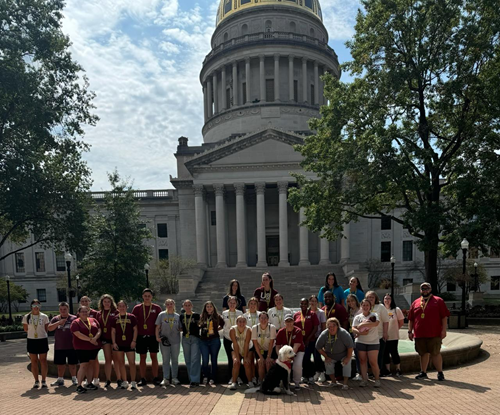 A group of 30 people stand in front of a domed building.