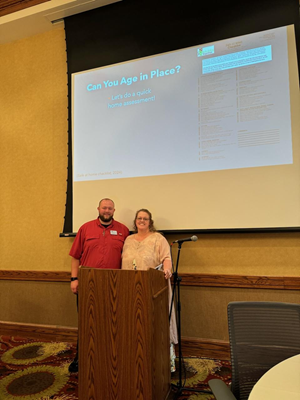 A woman and man pose in front of a projection screen.