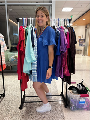 A woman stands in the middle of a rack of clothing, as if she is a piece of clothing on the rack.