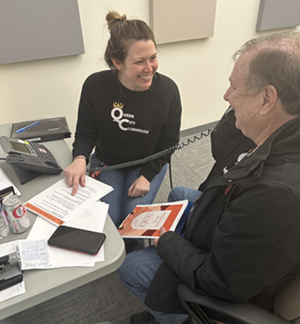 An elderly man holds a handset while a woman guides him through a telephone call.