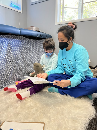 Dr. Smith and a young boy sit on the floor while reviewing a worksheet together.