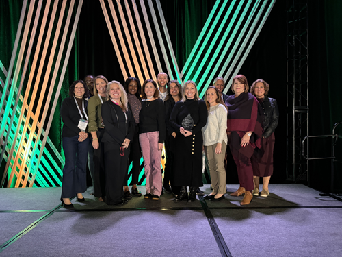 13 people pose on stage with an award